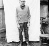 Foto nun exterior dun neno de pé, diante dunha saba que sostén un home tocado cunha pucha. 