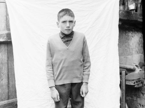 Foto nun exterior dun neno de pé, diante dunha saba que sostén un home tocado cunha pucha. 